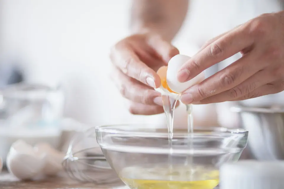 A freshly cracked egg in a shallow white bowl, with a round yolk standing in a clear, thick white.