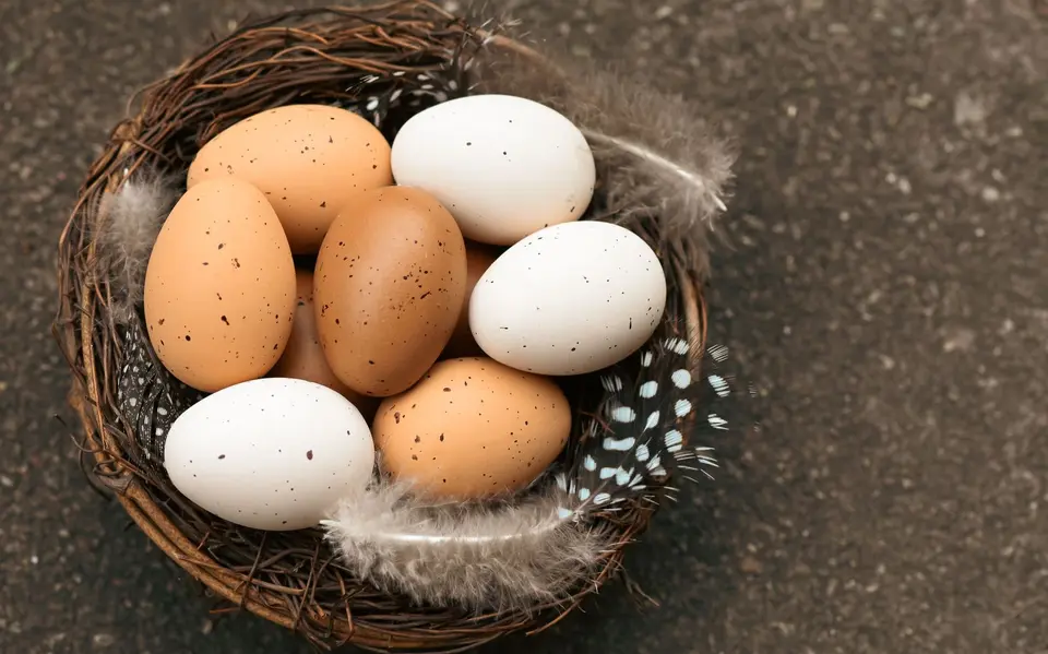 Brown, cream and white eggs in a woven basket, one cracked open to show an orange yolk.
