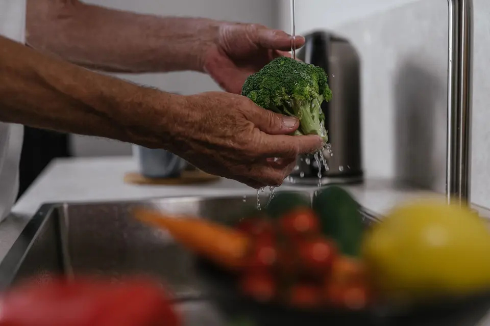 Fresh green leafy vegetables being rinsed under running water in a kitchen sink.