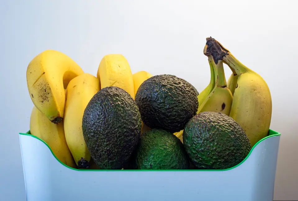 A brown paper bag holding a ripe banana and a firm green mango on a kitchen counter.