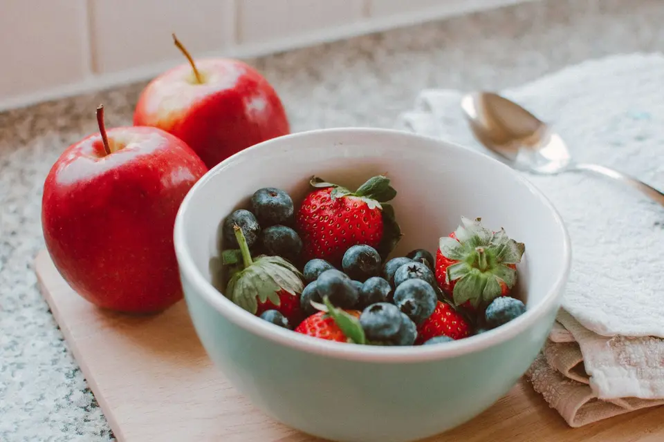 A bowl of bananas and mangoes on a counter next to a tray of berries ready for the fridge.