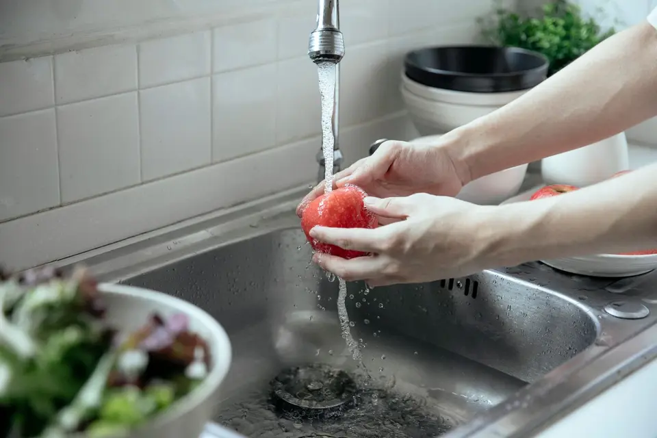 Red apples and oranges being rinsed under a gentle stream of water in a kitchen sink.