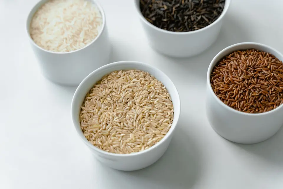 Two shallow bowls on a wooden table, one with brown rice and one with white rice, seen from above in daylight.
