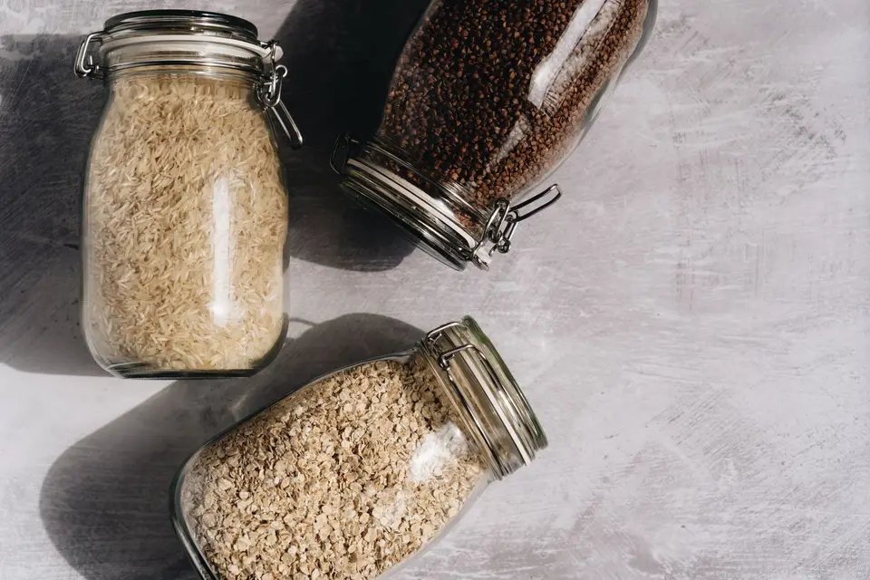 A sealed glass jar of white rice and a smaller jar of brown rice on a kitchen shelf, in soft daylight.