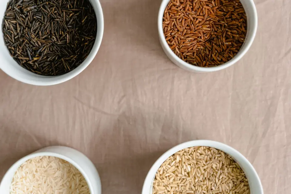 Small bowls of white jasmine rice, purple-black rice, red rice and white glutinous rice side by side on a table.
