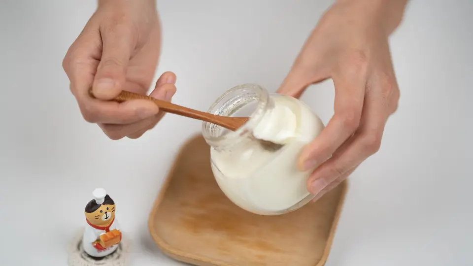 A refrigerator shelf holding a bottle of milk and a small tub of plain yogurt, with a thermometer beside them.