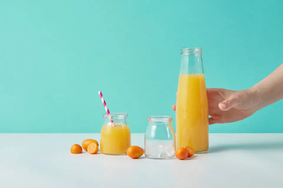Glass bottles of freshly pressed orange juice on a wooden table beside halved oranges.