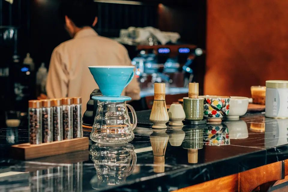 Small bowls of dried tea leaves and roasted coffee beans on a plain wooden surface.