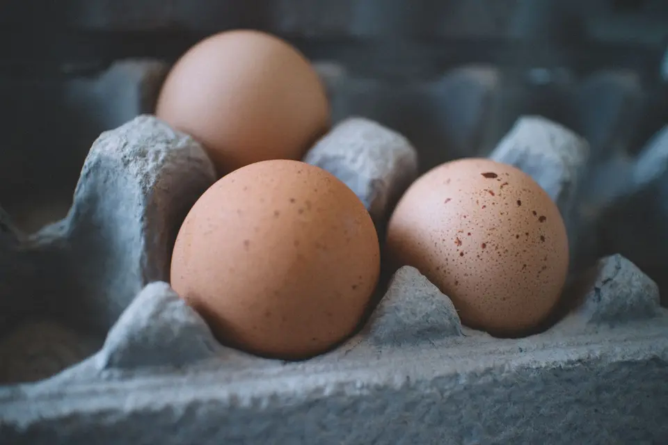 Ten brown eggs resting in a pressed-paper carton on a plain wooden table.