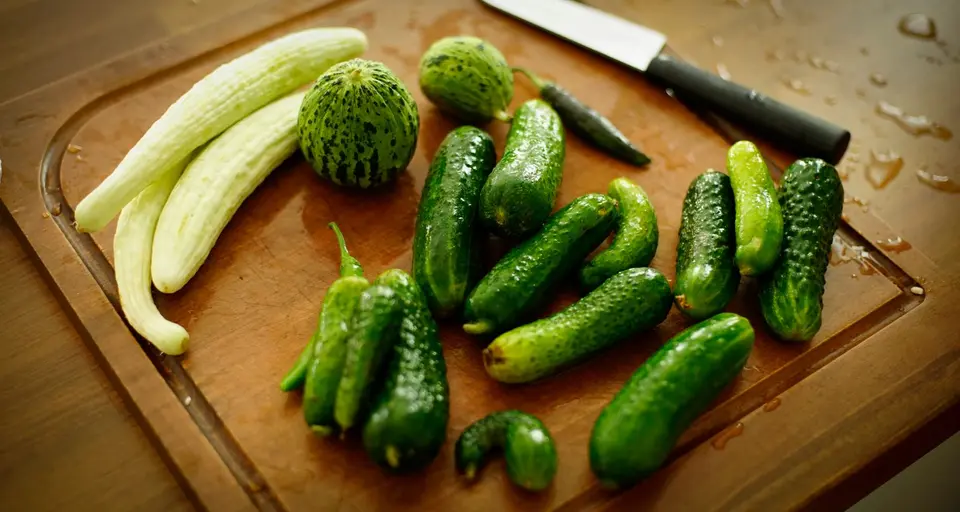 Whole and sliced green cucumbers on a wooden chopping board.