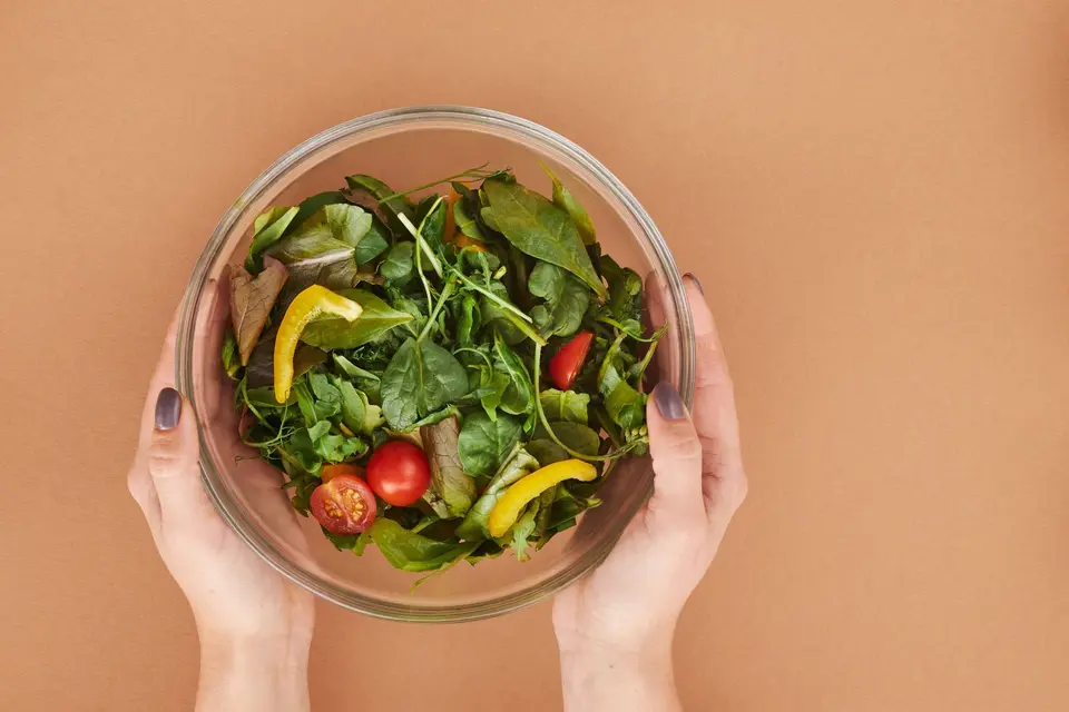 A white bowl of mixed green and red salad leaves in soft daylight.