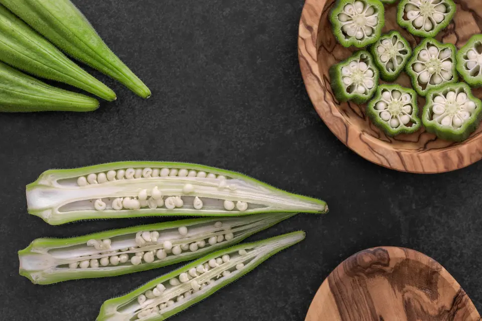 A pile of small green okra pods on a wooden board.