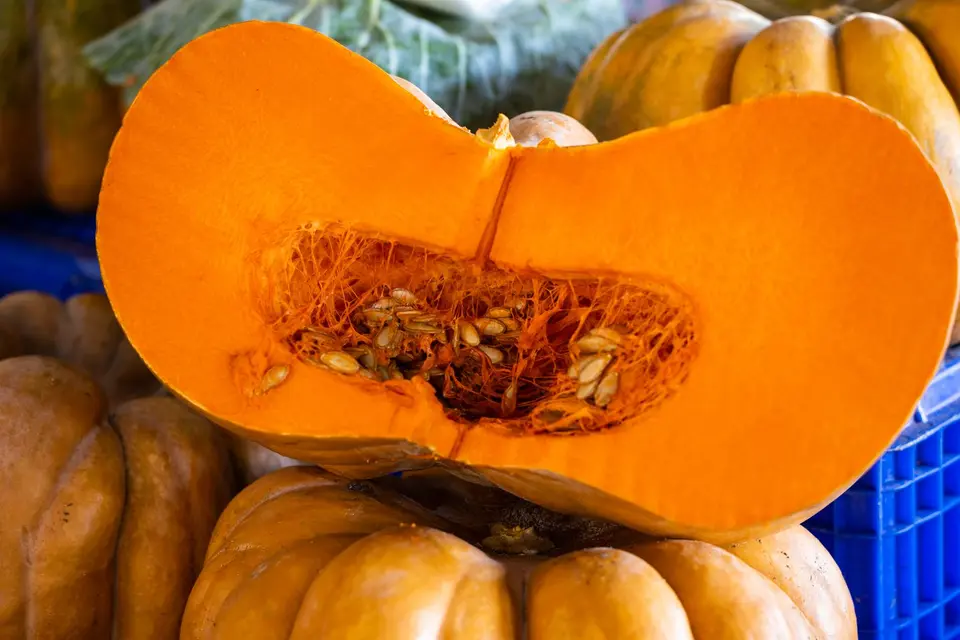 A pumpkin cut in half showing orange flesh and seeds on a kitchen board.