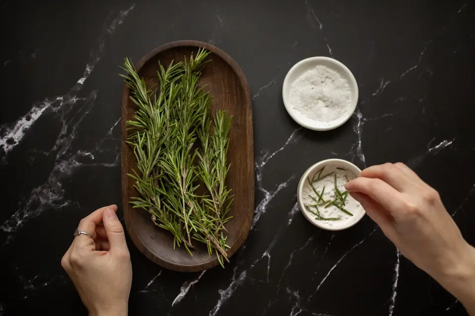Several sprigs of fresh rosemary with narrow green needles on a wooden table.