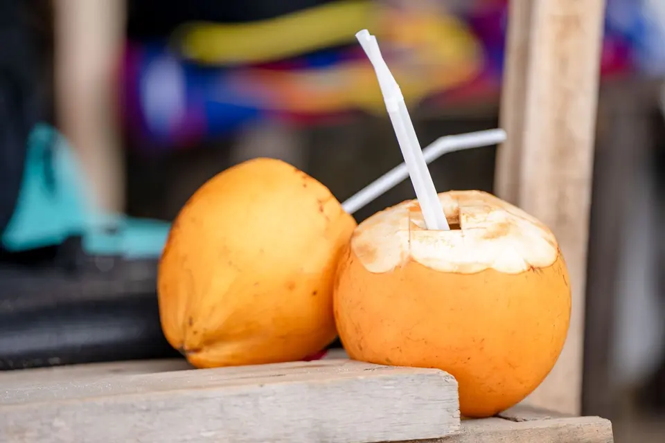A trimmed young coconut with a straw on a wooden table.