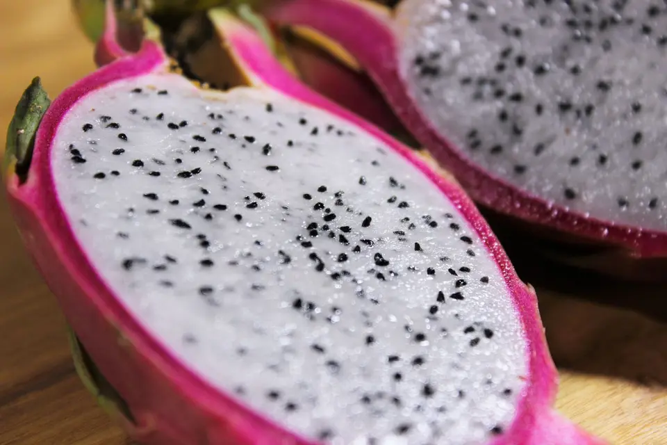 A dragon fruit cut in half showing speckled flesh and a pink skin with green tips.