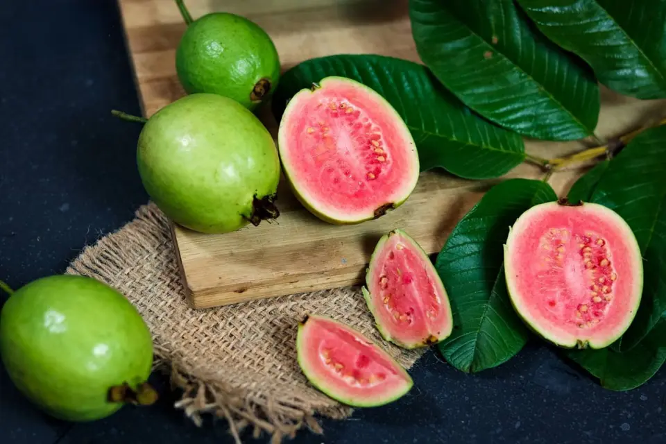 Whole and sliced green guavas with pale flesh on a wooden board.
