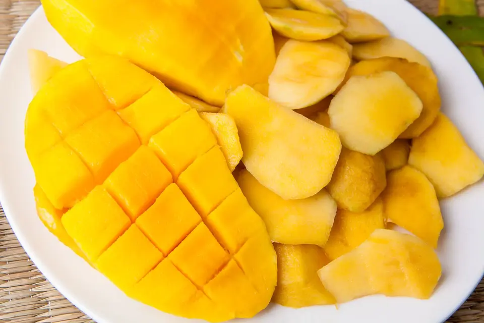A sliced golden mango with the flesh scored into cubes on a plain plate.
