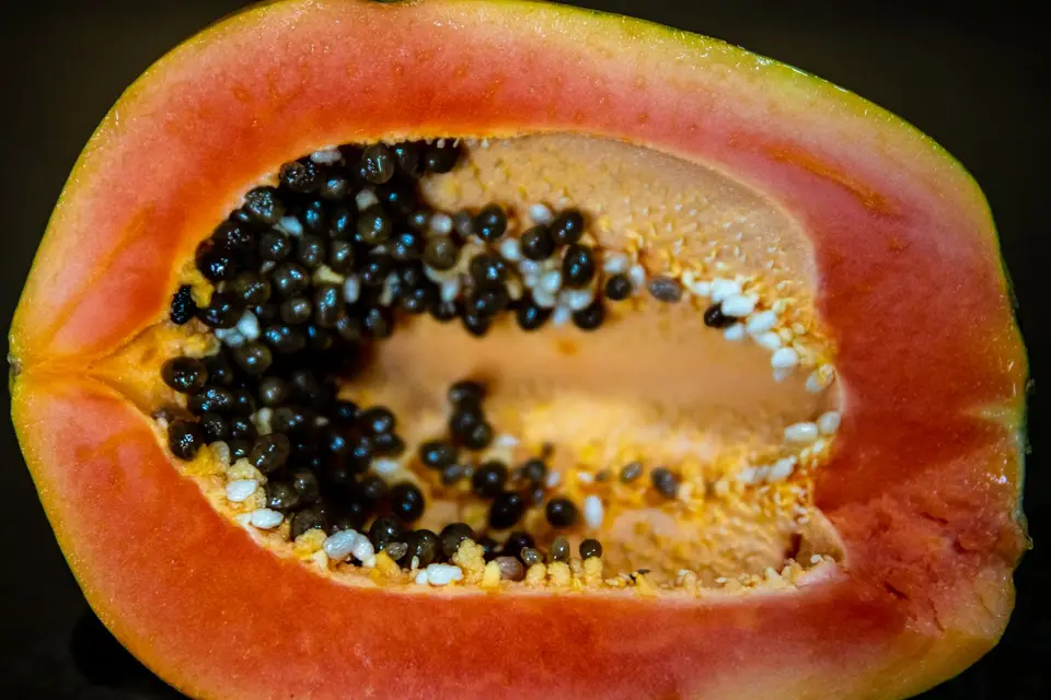A papaya cut in half showing orange flesh and black seeds on a plate.