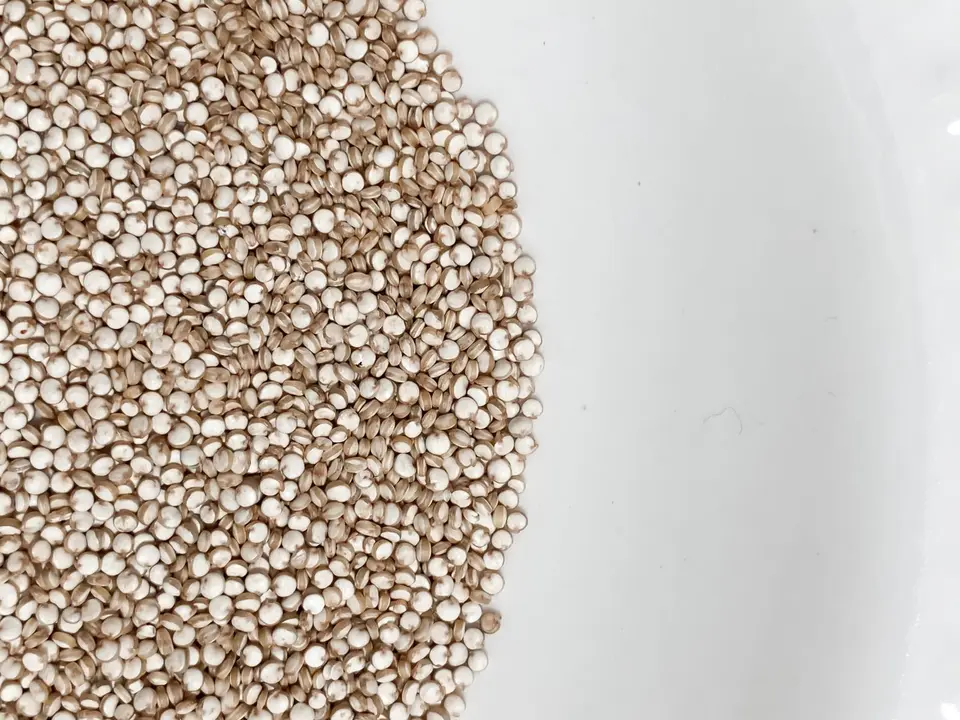 A wooden bowl of pale, dry quinoa grains on a plain linen cloth.