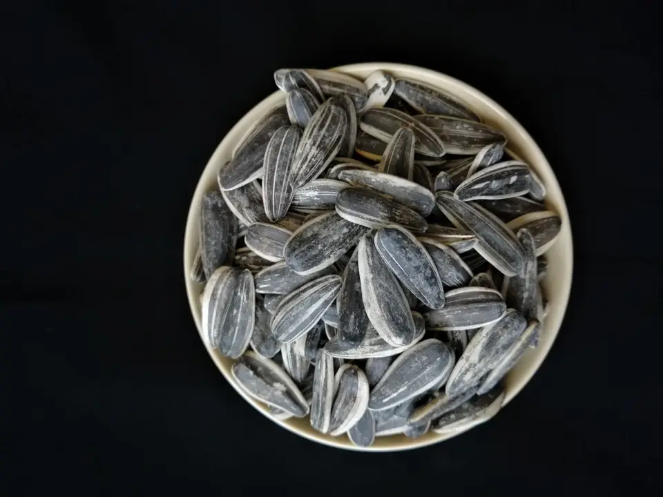 A shallow bowl of pale, shelled sunflower seeds on a rustic wooden board.
