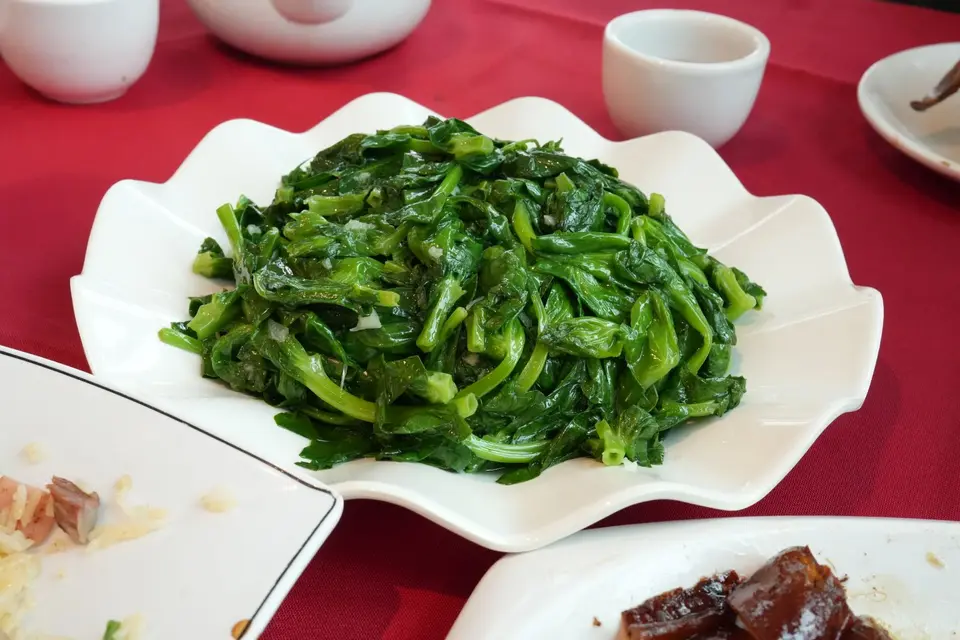 Green Chinese kale stems and leaves stir-fried with garlic on a white plate.