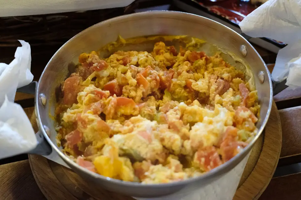 A shallow bowl of scrambled egg and red tomato pieces in a glossy sauce, next to steamed rice.