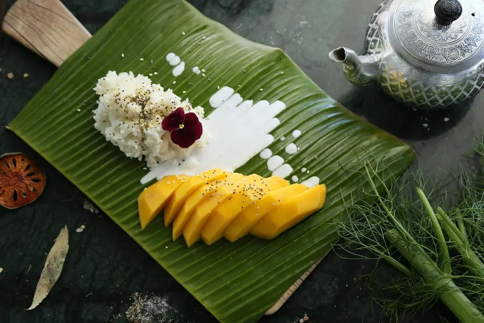 A plate of sliced yellow mango beside a mound of white sticky rice with coconut cream poured on top.