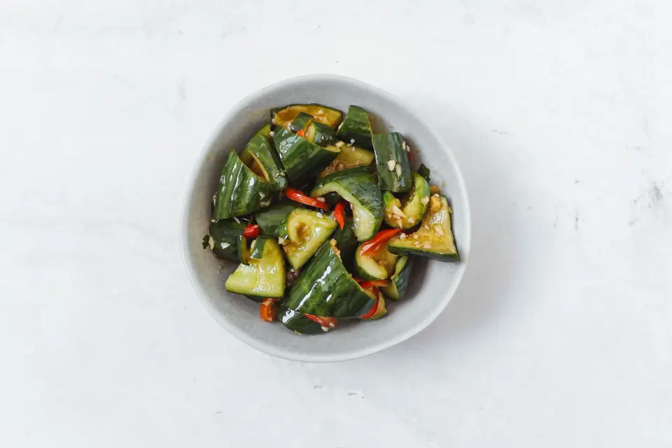 A bowl of cracked cucumber pieces with halved cherry tomatoes, chilli and crushed peanuts.