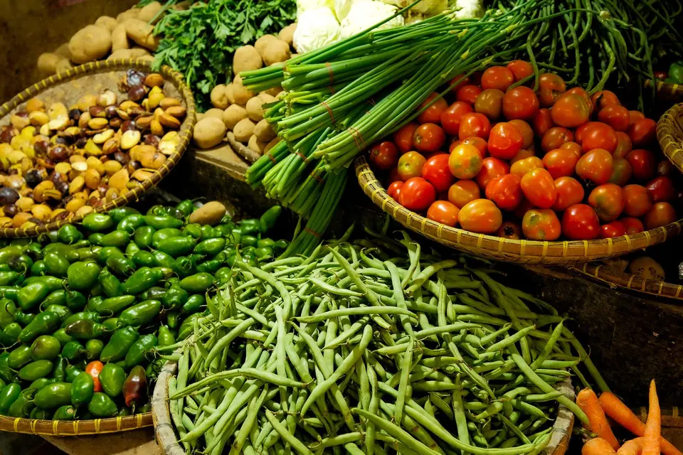 A basket of fresh vegetables beside bags of rice and dried beans on a kitchen counter.