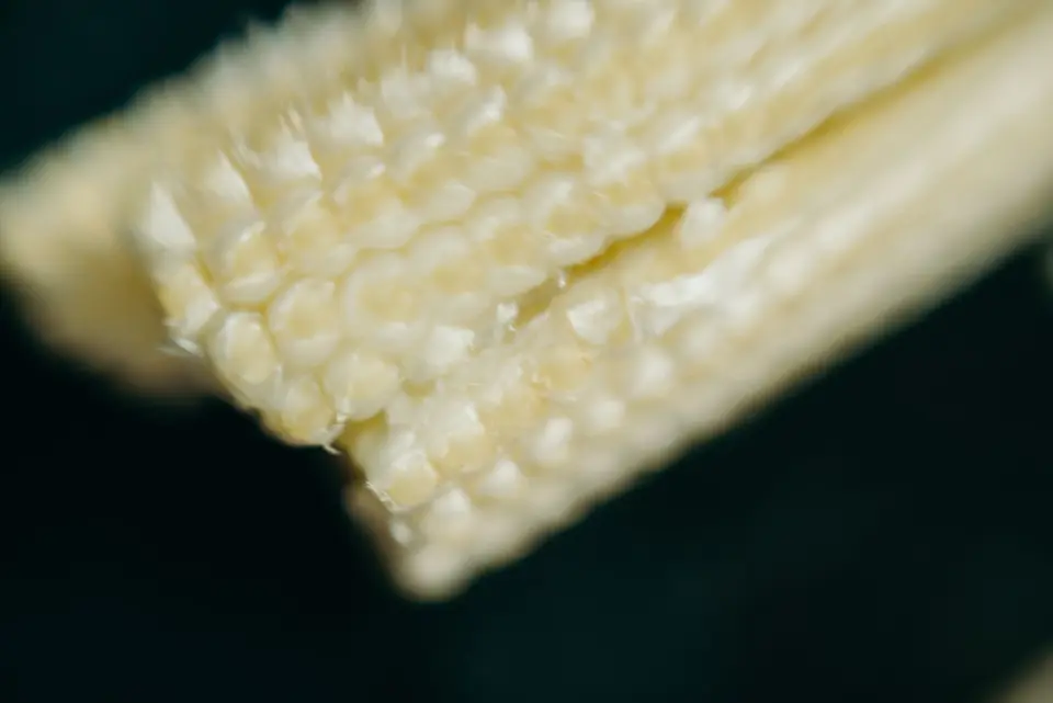 A handful of small pale yellow baby corn cobs on a wooden board.