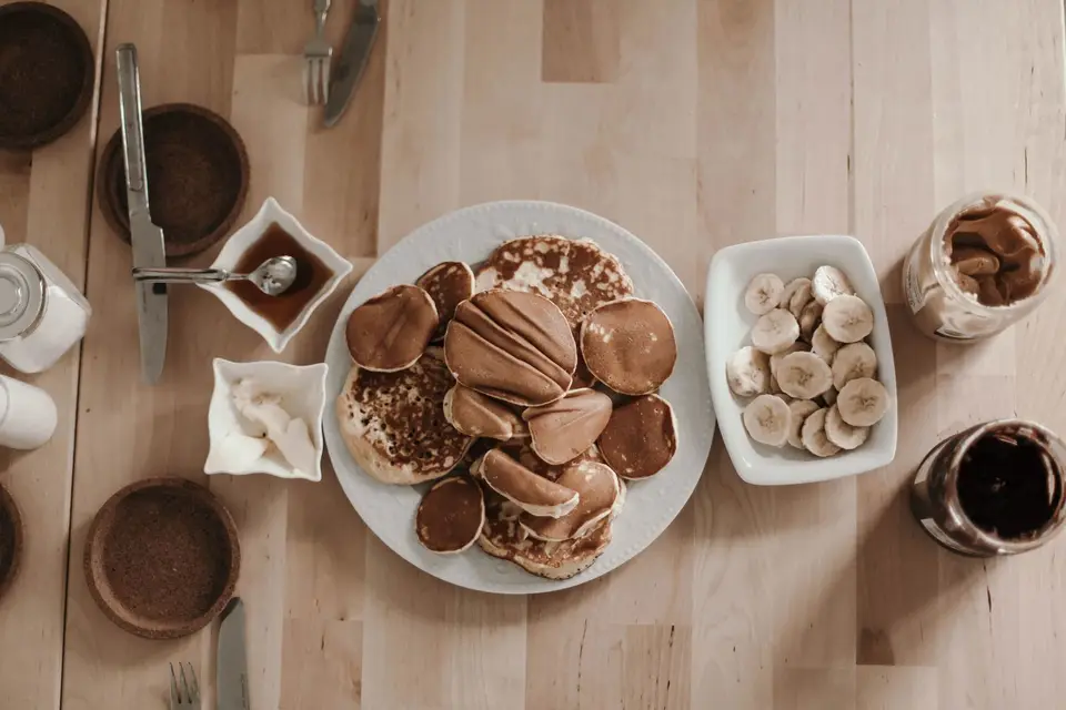 A stack of small golden pancakes with banana slices on a plain plate.