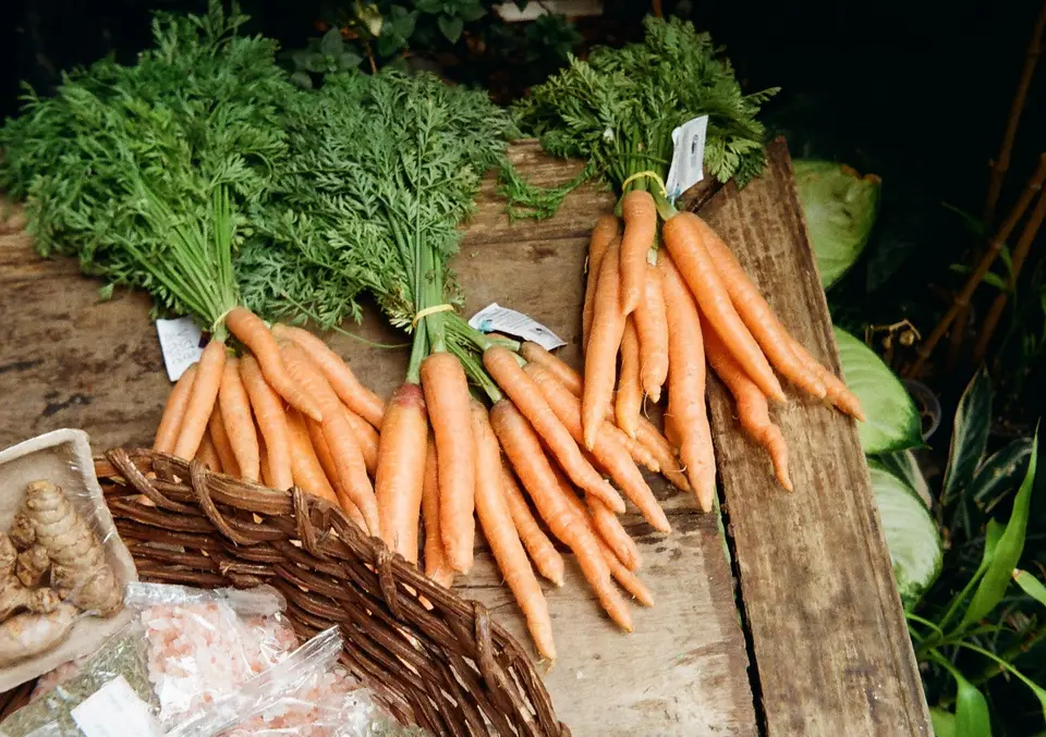 A pile of orange carrots with a few green tops on a wooden table.