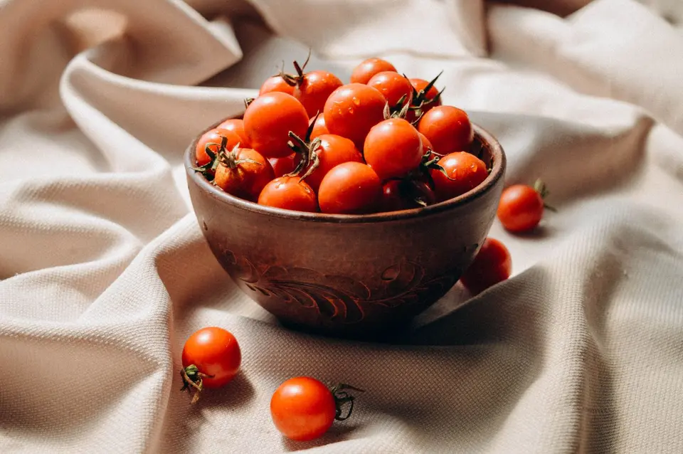 A small bowl of red cherry tomatoes with a few still on the vine.