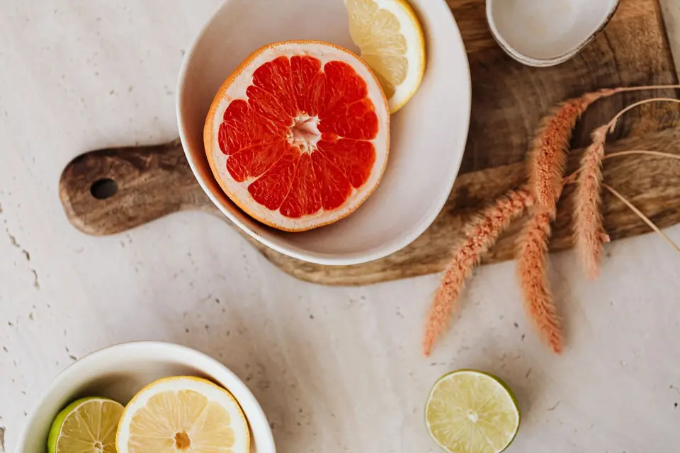 A bowl of sliced pale fruit with a halved lemon beside it on a wooden board.