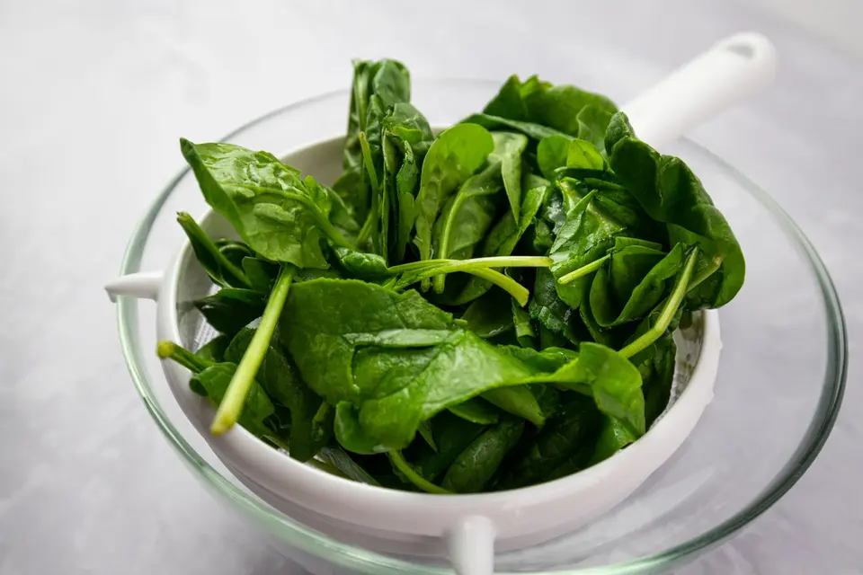 A bowl of small, bright green baby spinach leaves on a white table.