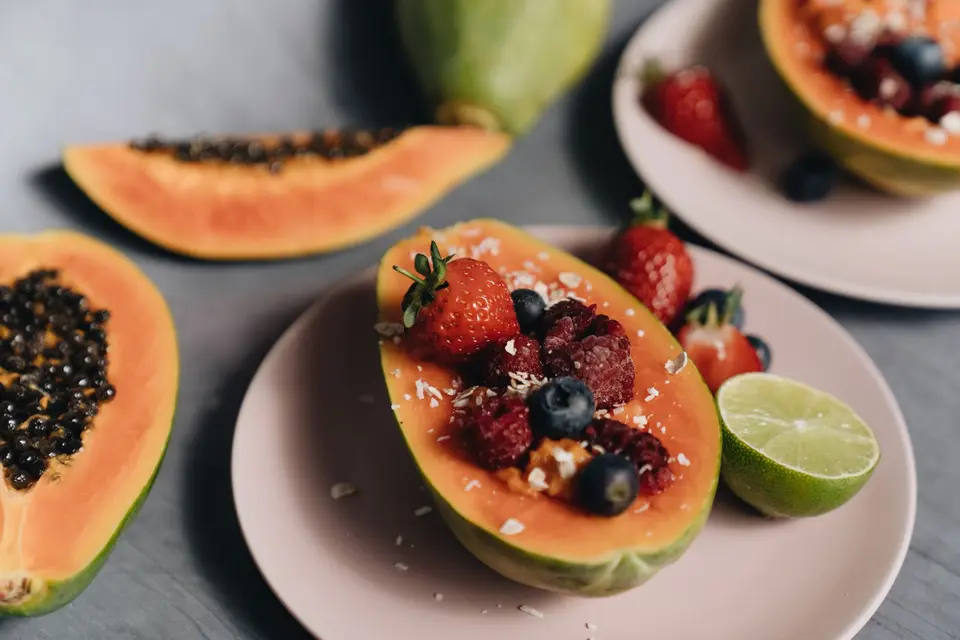 Ripe papaya halves filled with strawberries and blueberries, with a halved lime on the plate.